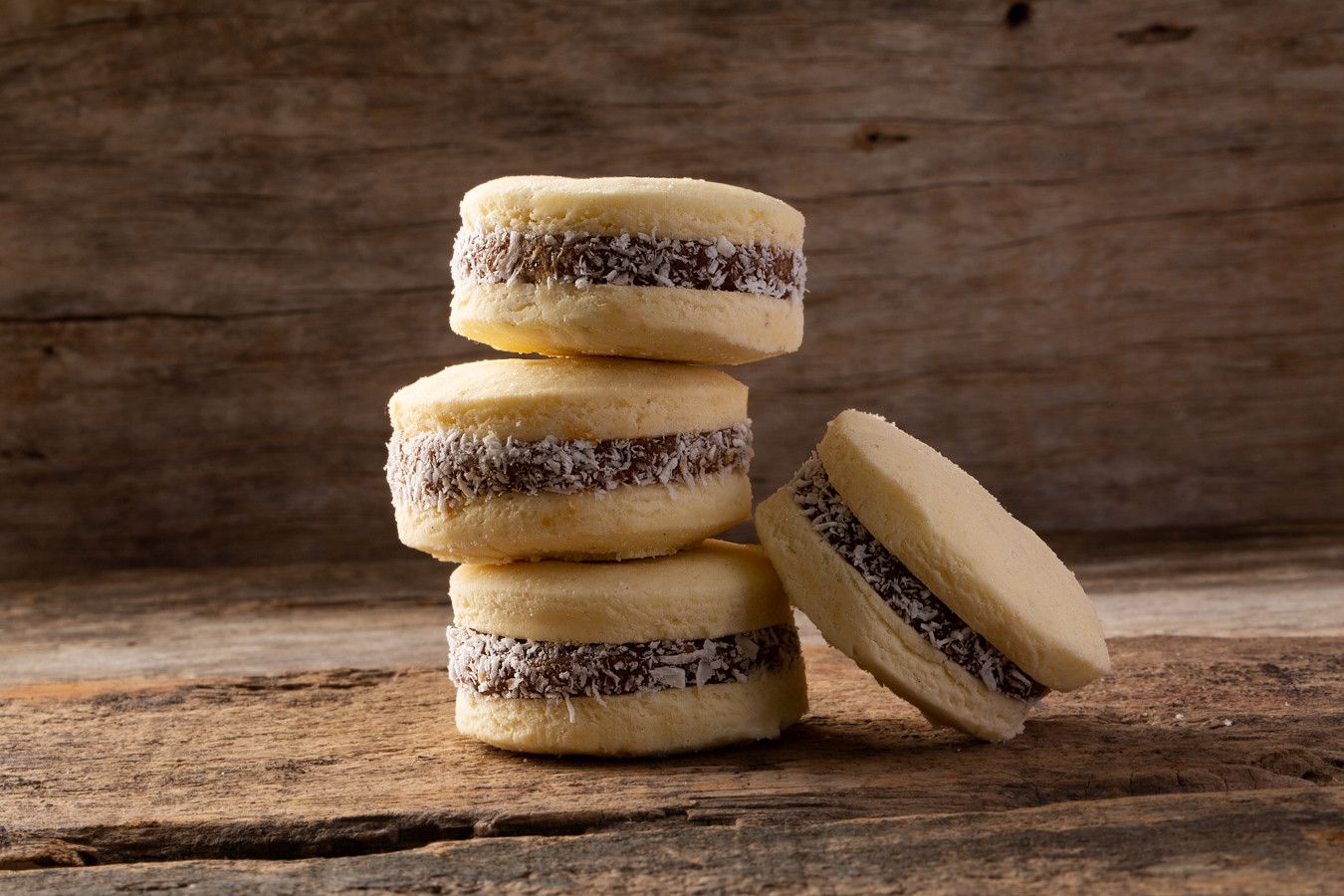 Biscoitos recheados empilhados sobre uma superfície rústica de madeira, com um biscoito inclinado para a frente.