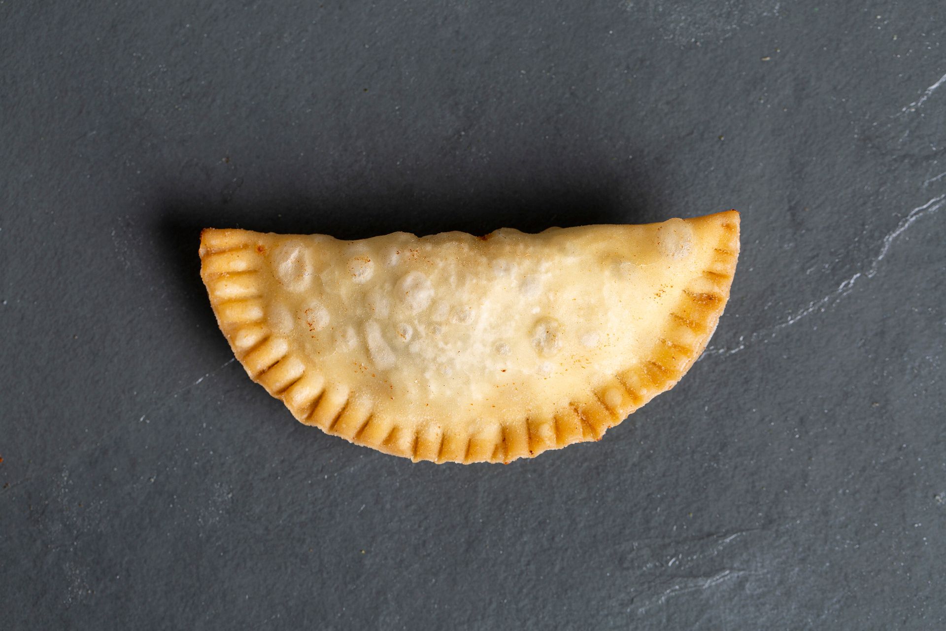 Pastel frito em formato de meia-lua com borda frisada sobre uma superfície de pedra escura.