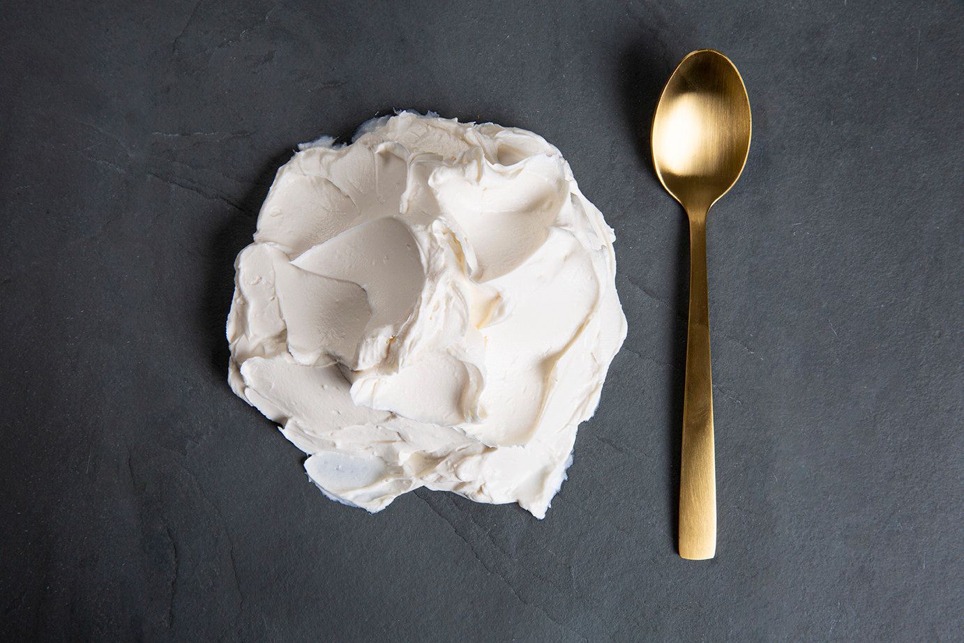 Creme branco ou glacê sobre uma superfície escura ao lado de uma colher dourada.