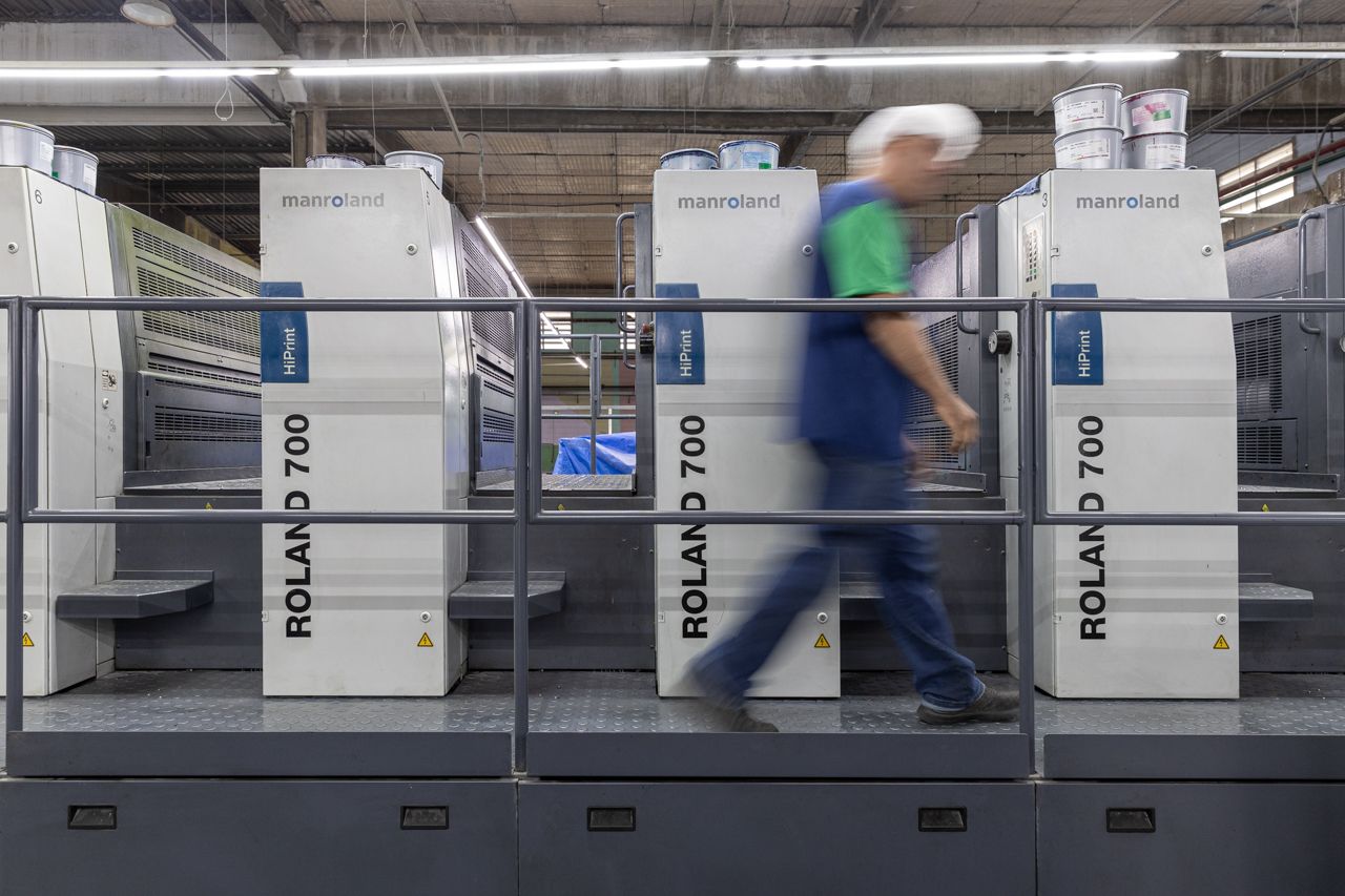 Operário passando por grandes máquinas industriais brancas em um ambiente fabril.