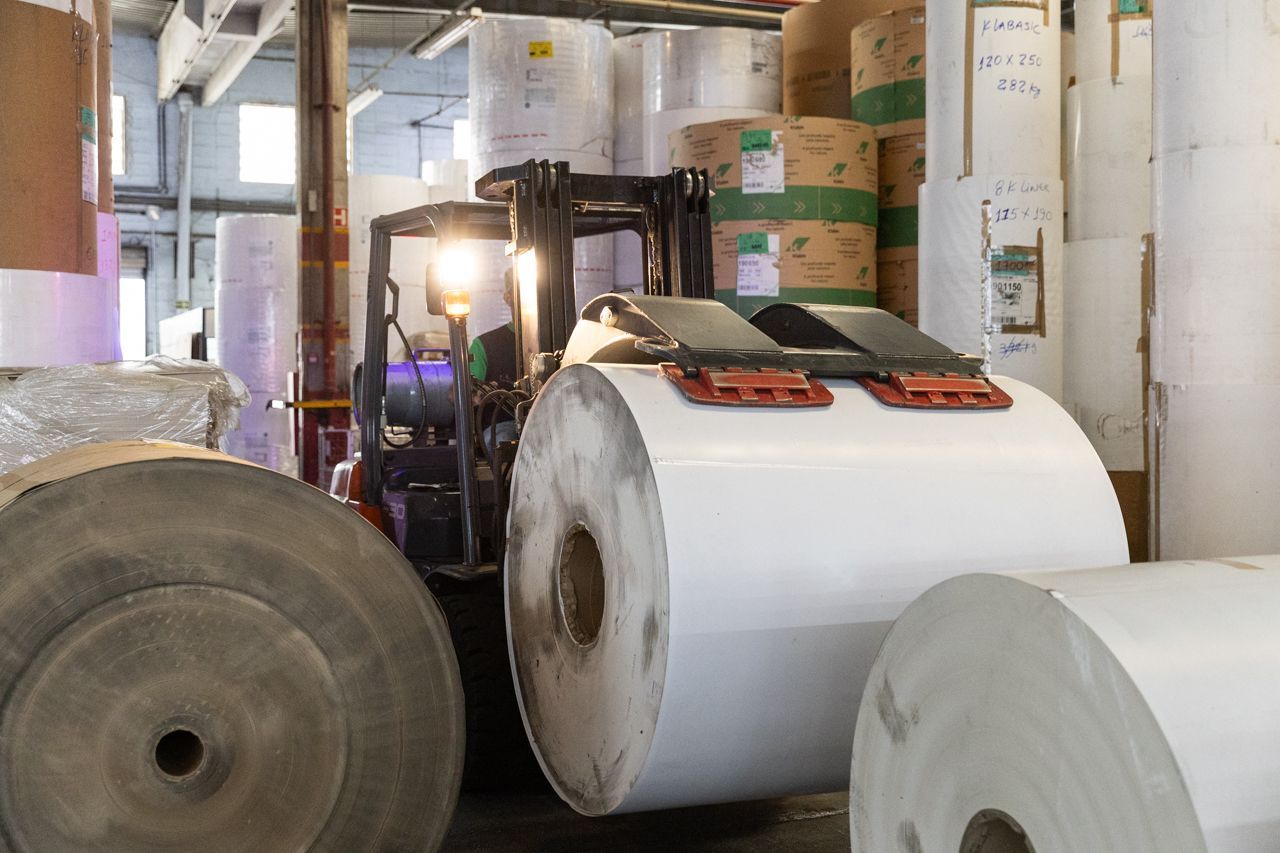 Empilhadeira em um armazém movimentando grandes rolos de papel e materiais de embalagem de papelão.
