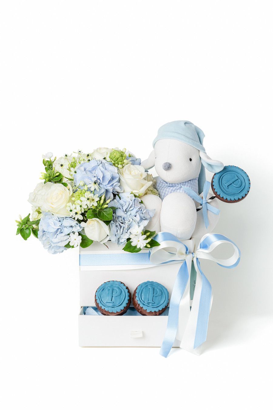Conjunto de presente para bebê em azul e branco com flores, ursinho de pelúcia e fita, dentro de uma caixa branca.