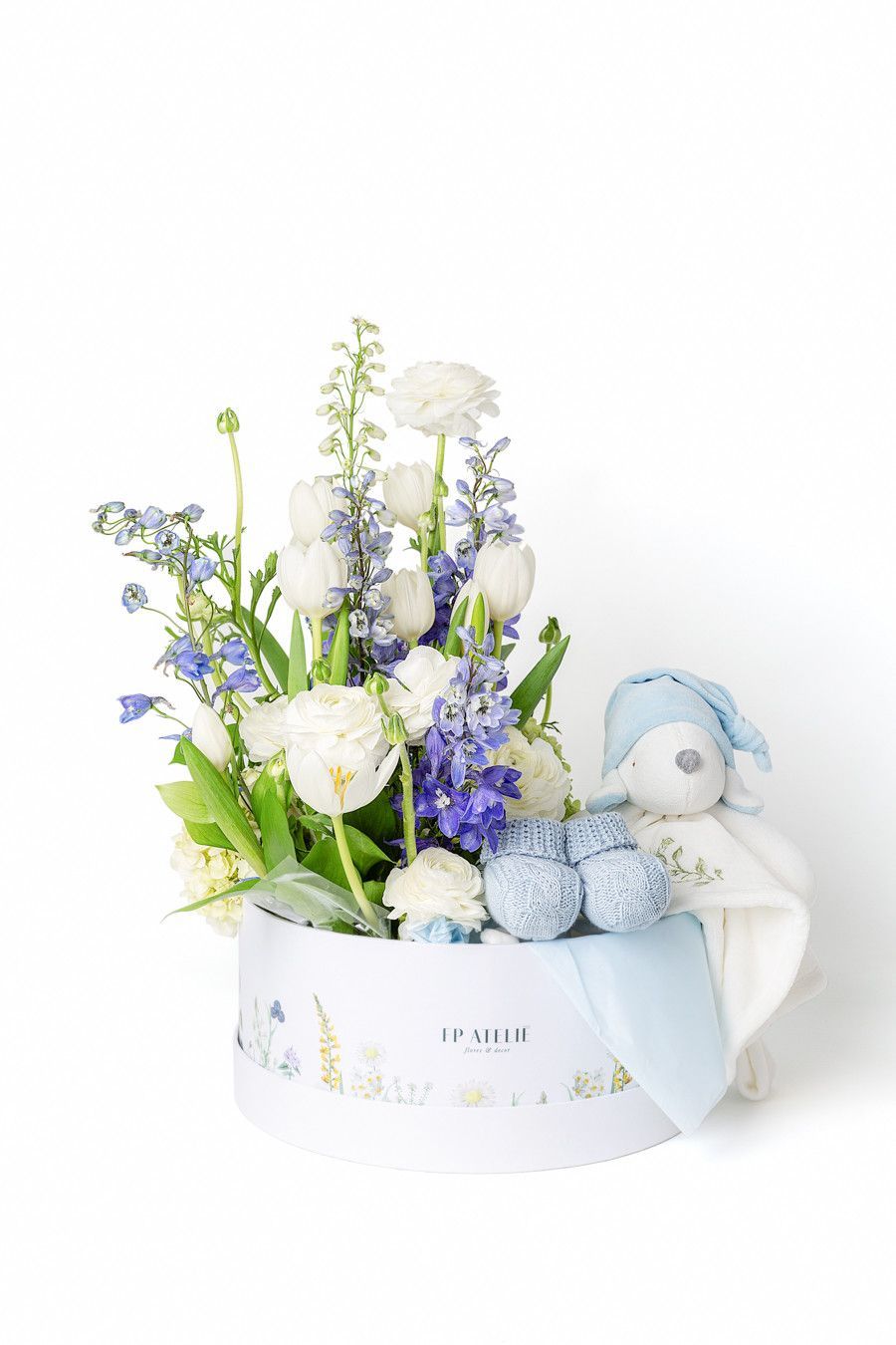 Arranjo floral azul e branco em caixa redonda com um pequeno brinquedo de pelúcia.