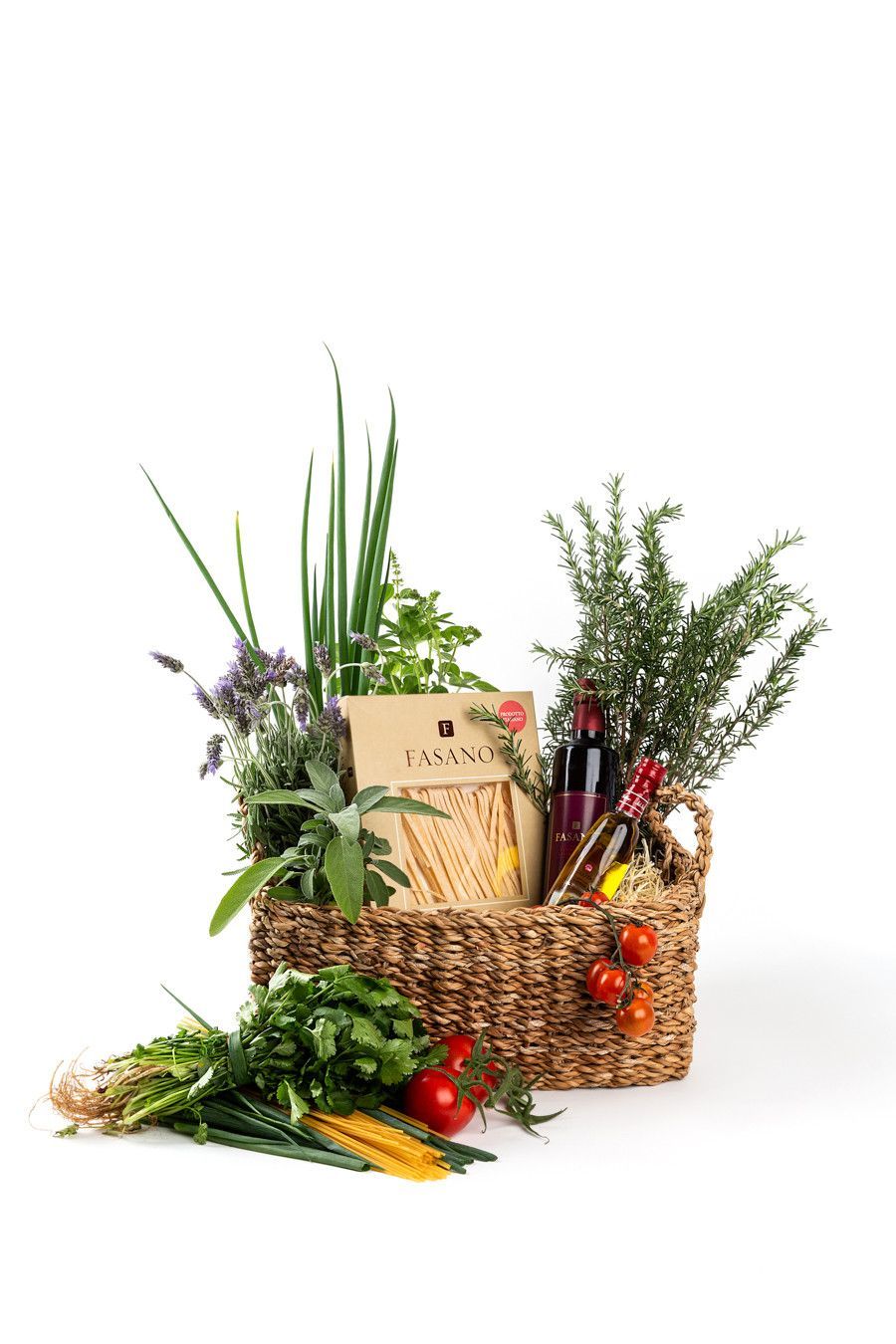 Cesta de vime para presentes com flores, folhagens, frutas e um cartão sobre fundo branco.