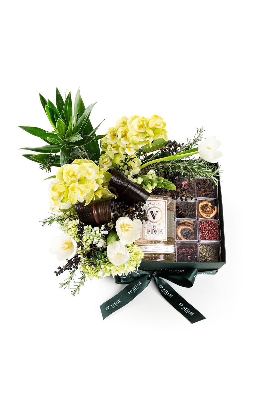 Cesta de presente com flores amarelas, folhagem verde, chocolates e um laço de fita escura.