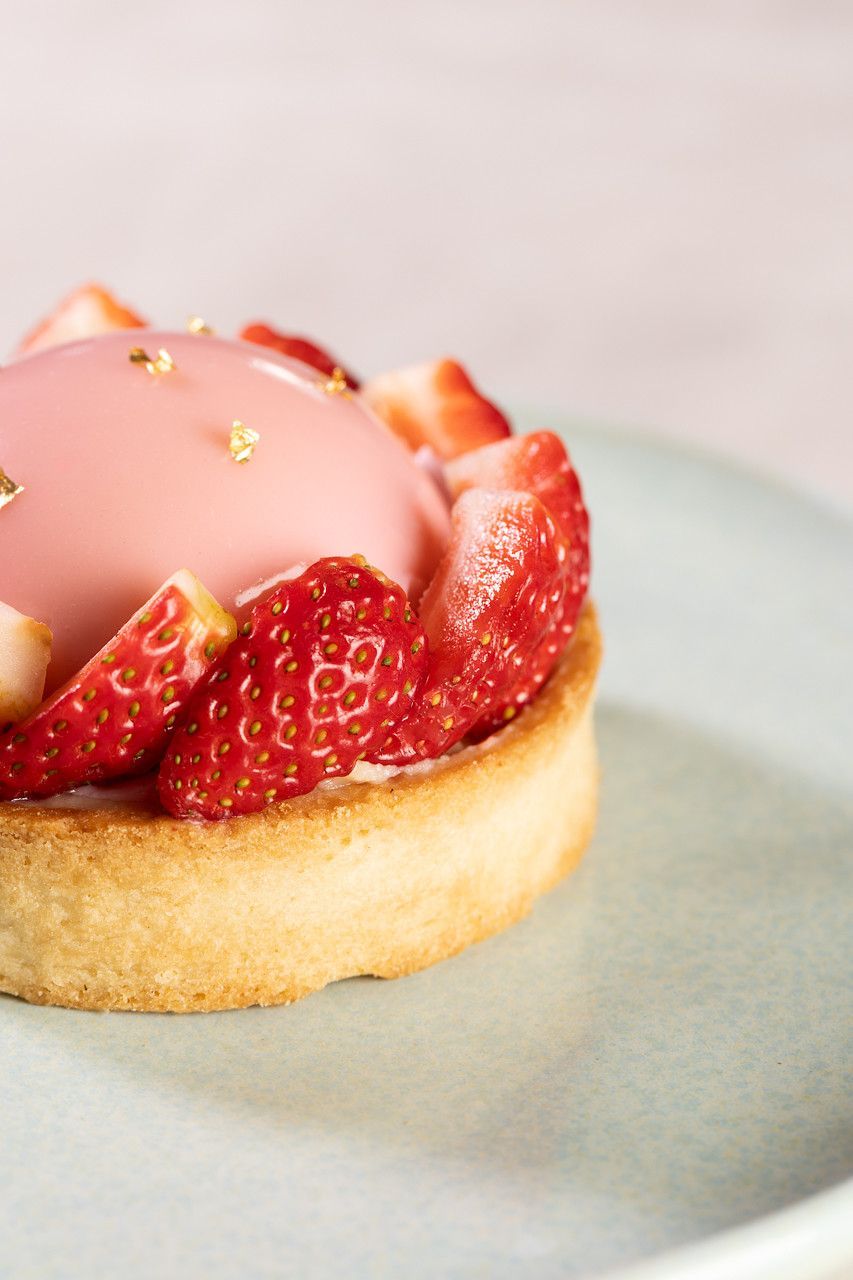 Tarte de morango com cobertura rosa e granulado dourado servida em um prato.