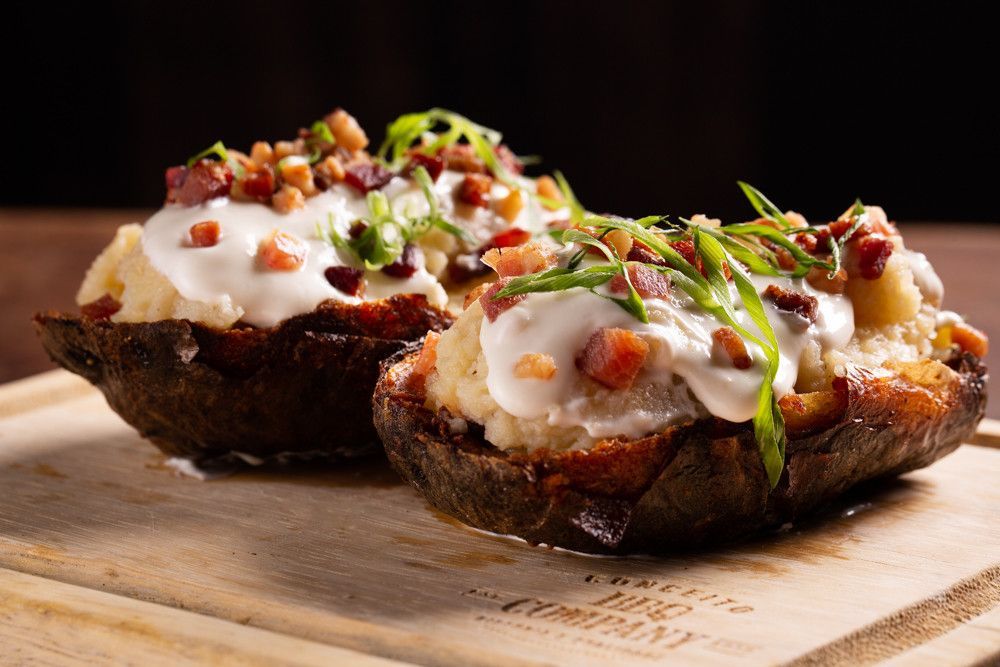 Batatas assadas recheadas com creme azedo, bacon e cebolinha, servidas em uma tábua de madeira.