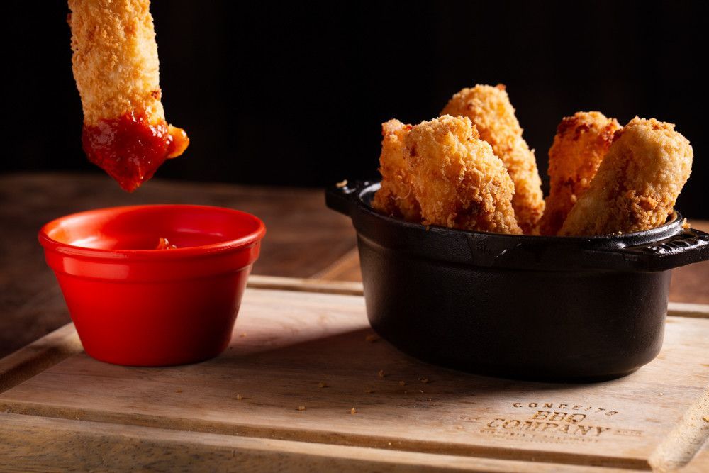 Nuggets de frango com molho vermelho servidos em copinhos numa tábua de madeira.