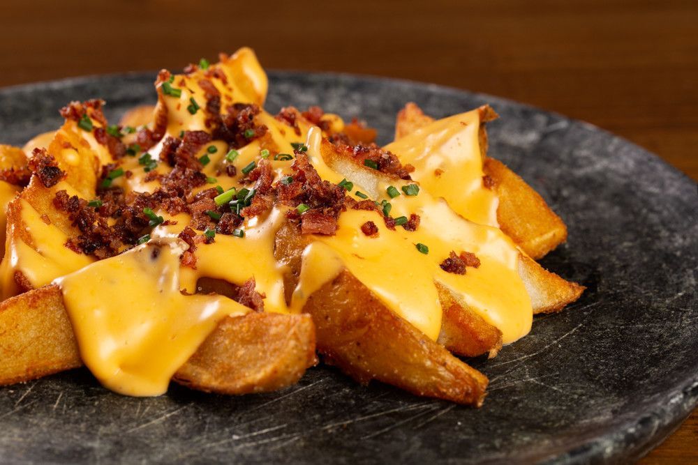 Batatas rústicas recheadas com queijo derretido, bacon em pedaços e cebolinha, servidas em um prato escuro.