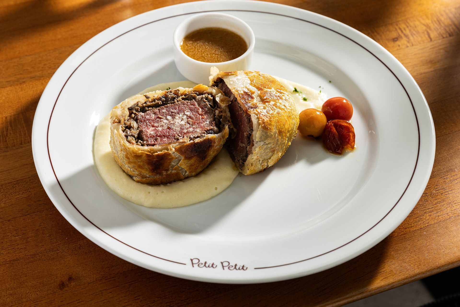 Carne Wellington servida com molho e morangos em um prato branco.