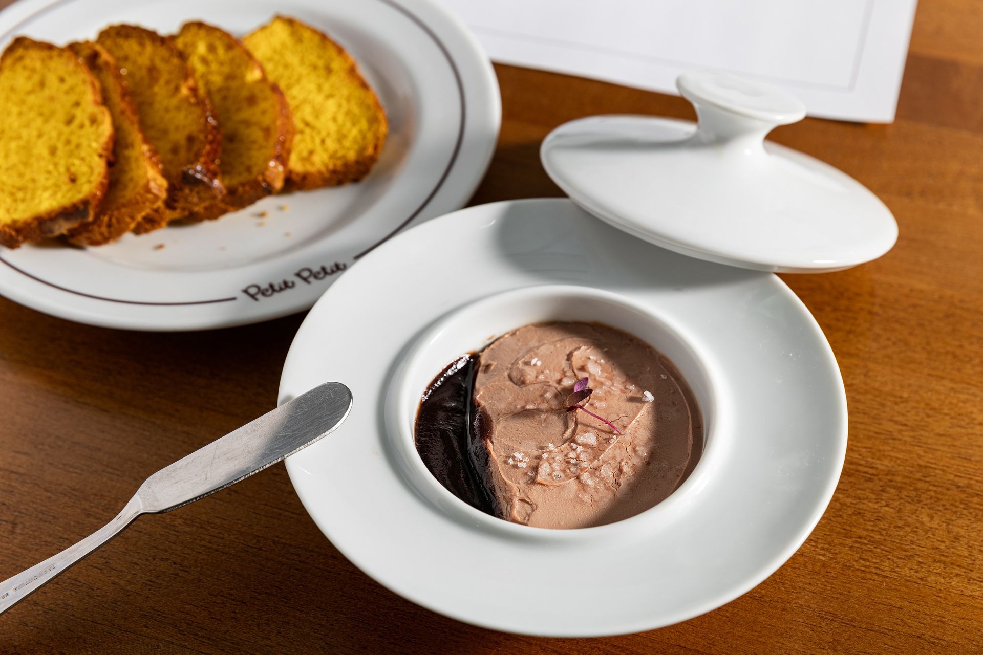 Tigela de sorvete de chocolate com colher ao lado de fatias de bolo em um prato branco.