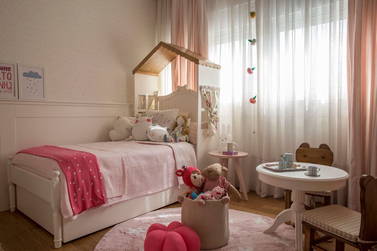 Quarto infantil rosa com cama, dossel, bichinhos de pelúcia e uma pequena mesa redonda junto à janela.