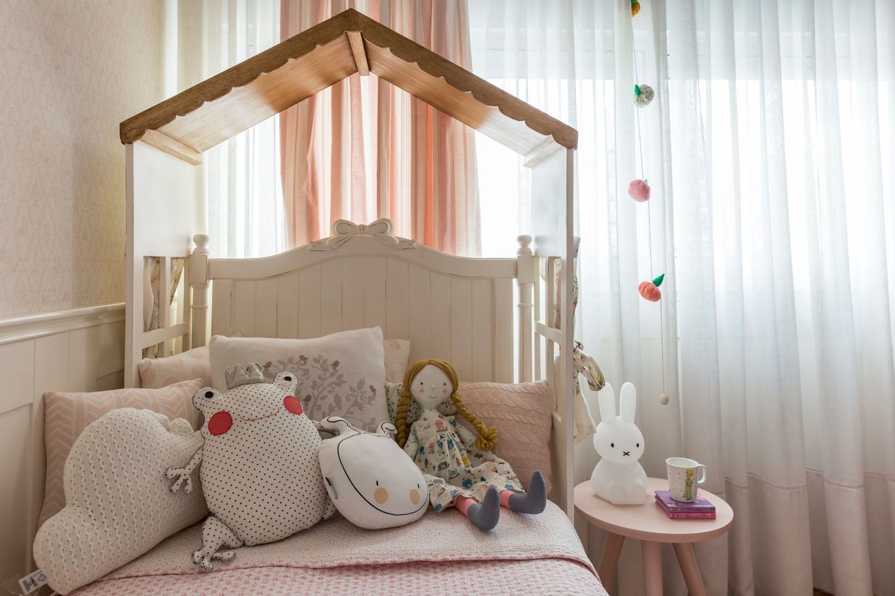 Cama infantil aconchegante com bichinhos de pelúcia e um abajur em forma de coelho sob um dossel de madeira junto a uma janela bem iluminada.