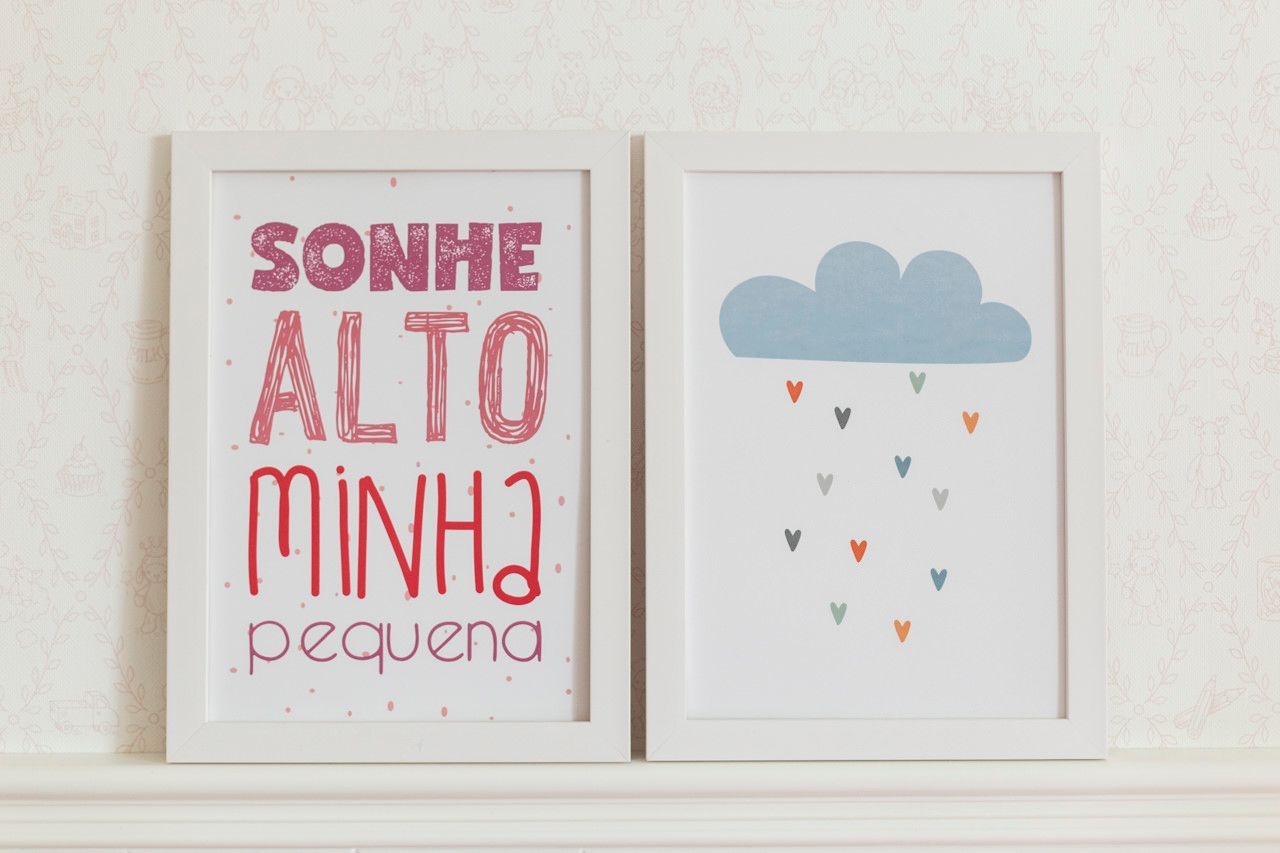 Duas gravuras emolduradas em uma prateleira: uma com a inscrição rosa “SONHE ALTO MINHA pequena” e outra com uma nuvem com gotas de chuva coloridas.