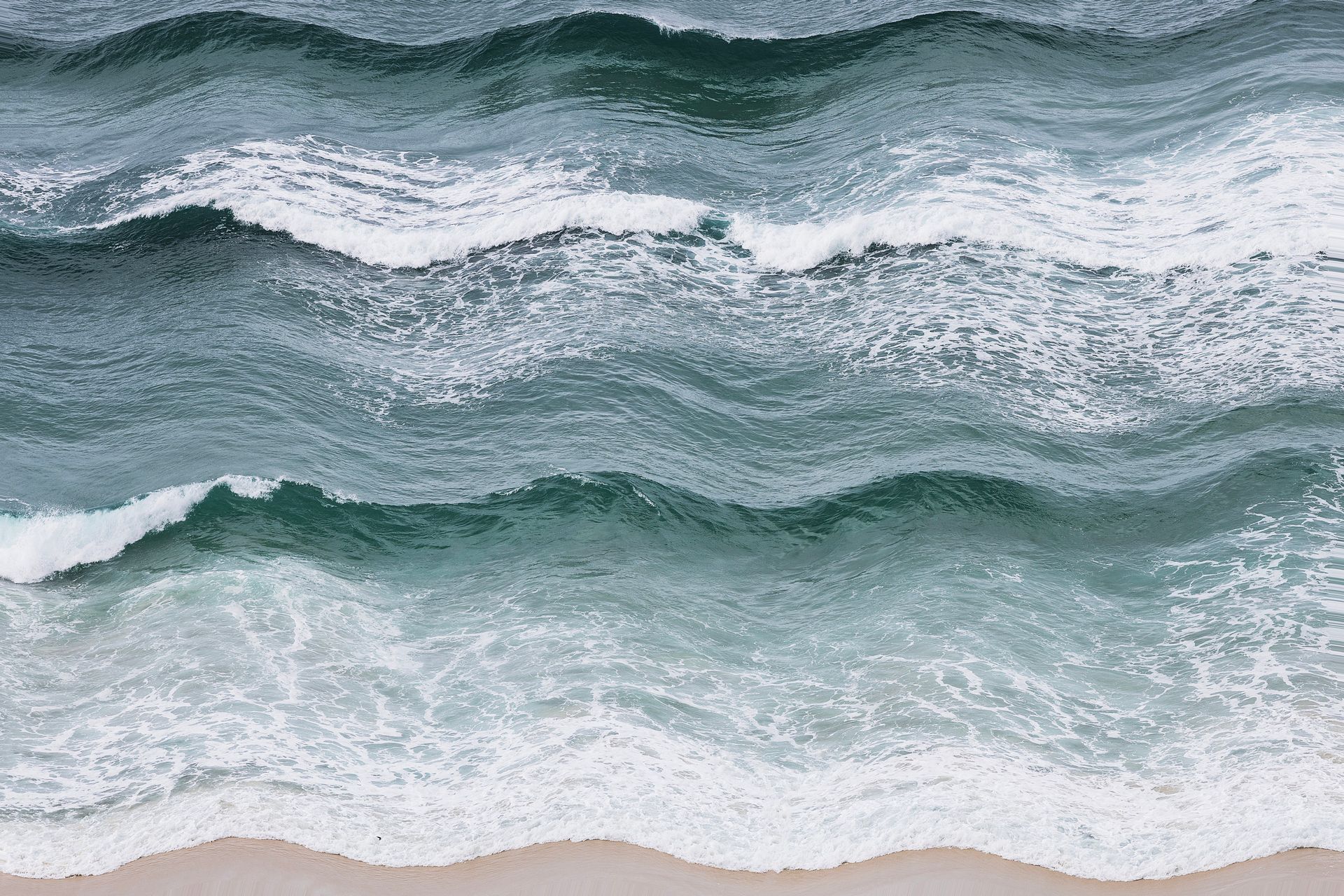 Ondas quebrando na praia de areia, com espuma branca e água azul-turquesa.