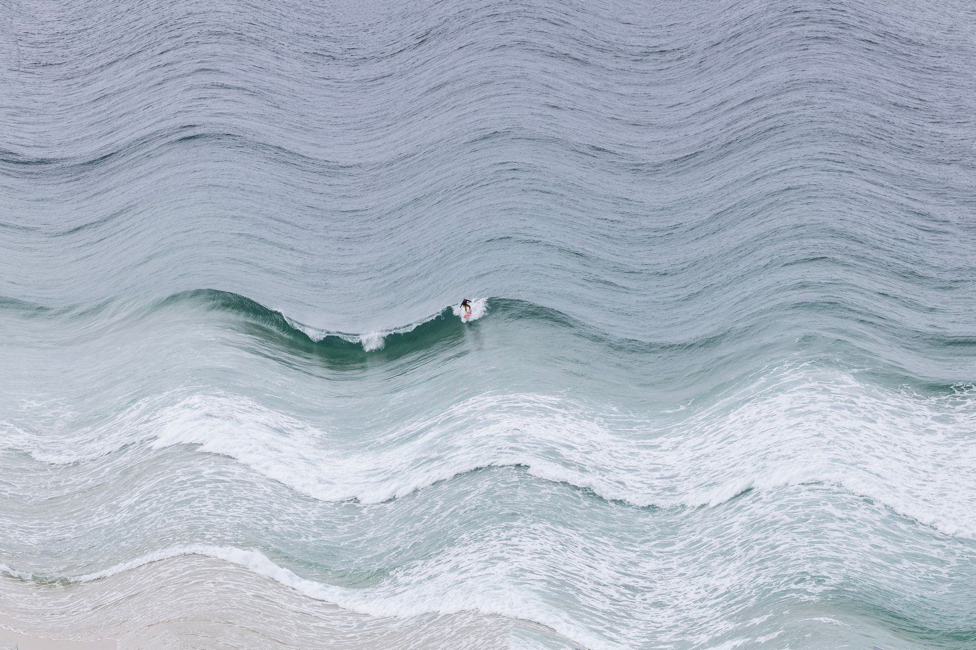 Vista aérea de um surfista solitário deslizando sobre uma onda verde no oceano.