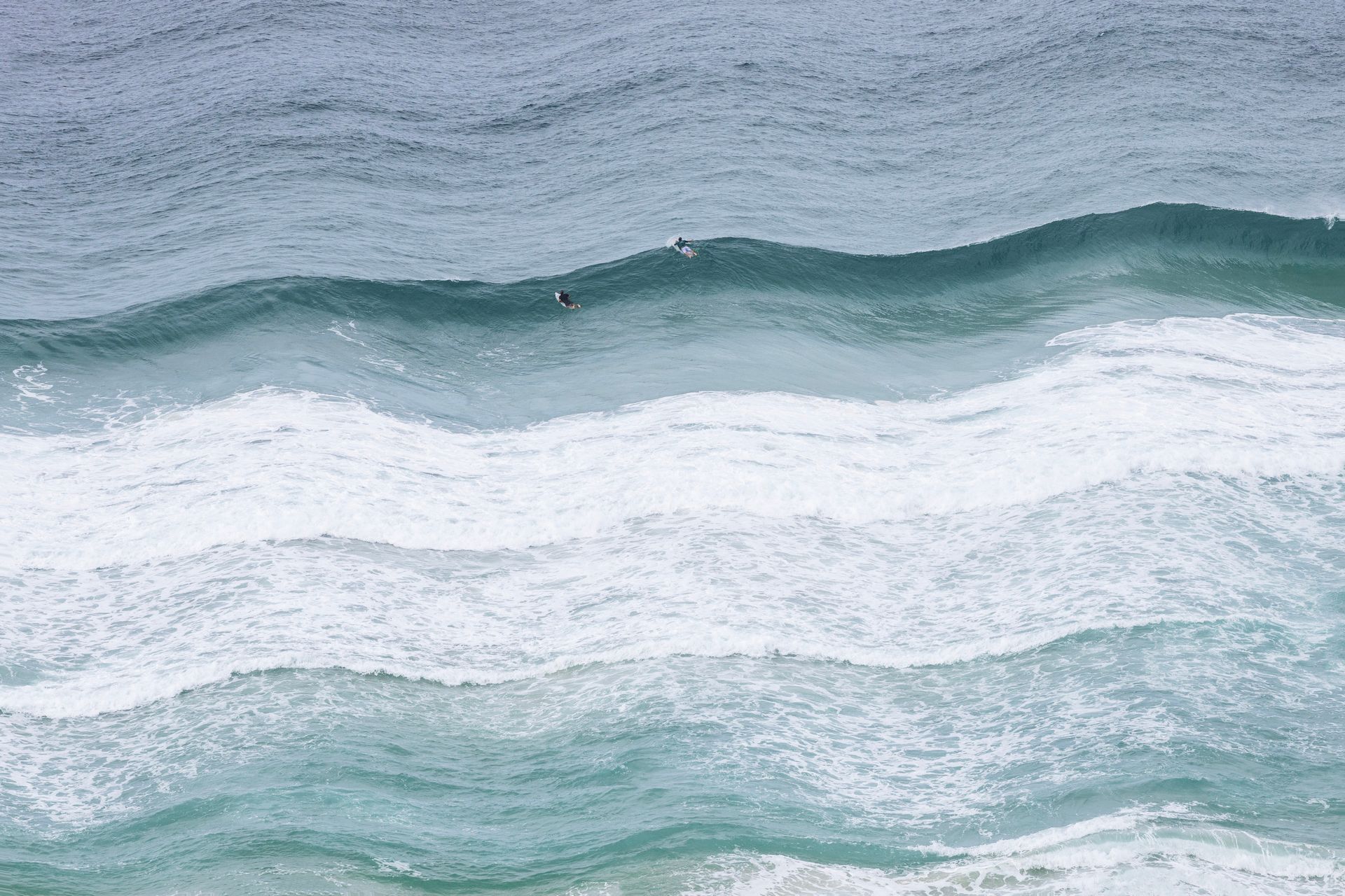 Ondas agitadas do oceano com espuma branca e água azul-turquesa sob um céu nublado.