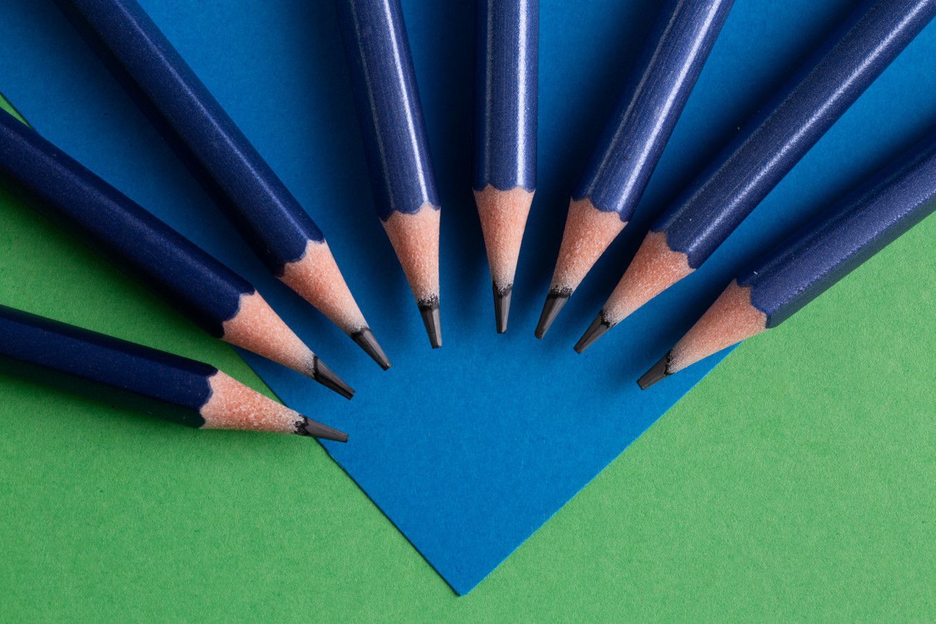 Lápis azuis dispostos em leque ao redor de uma forma de papel azul sobre um fundo verde.