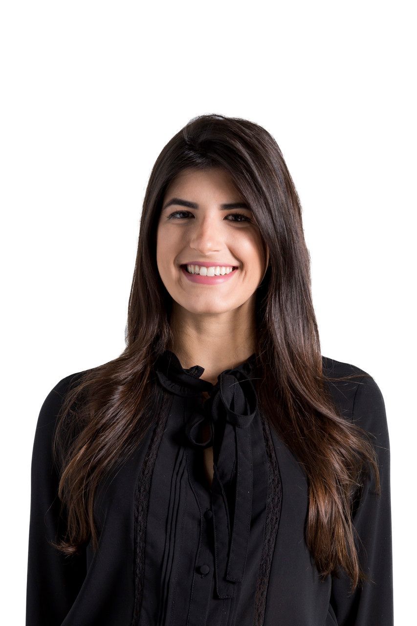 Retrato de uma mulher sorridente com longos cabelos escuros, vestindo uma blusa preta, sobre um fundo branco.