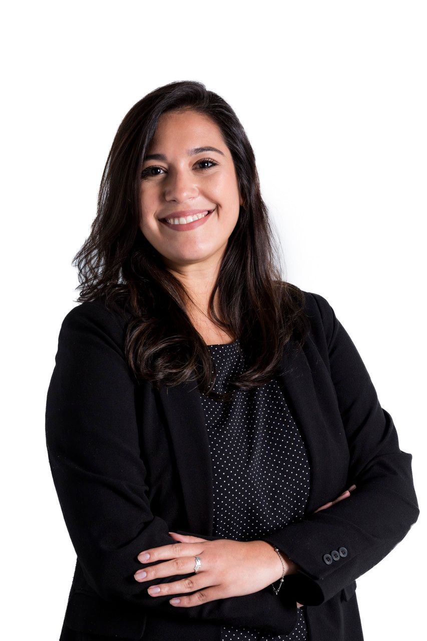 Mulher sorridente de blazer preto com os braços cruzados contra um fundo branco.