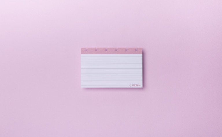 Bloco de notas rosa com linhas, centralizado em um fundo rosa pastel com uma leve sombra.