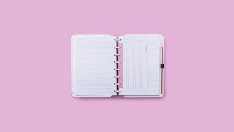 Caderno espiral aberto com páginas pautadas sobre fundo rosa.