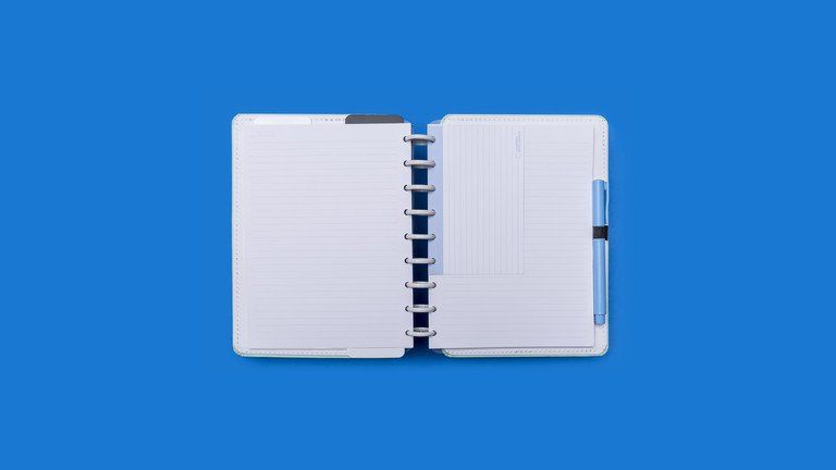 Caderno espiral aberto com capa azul sobre fundo azul