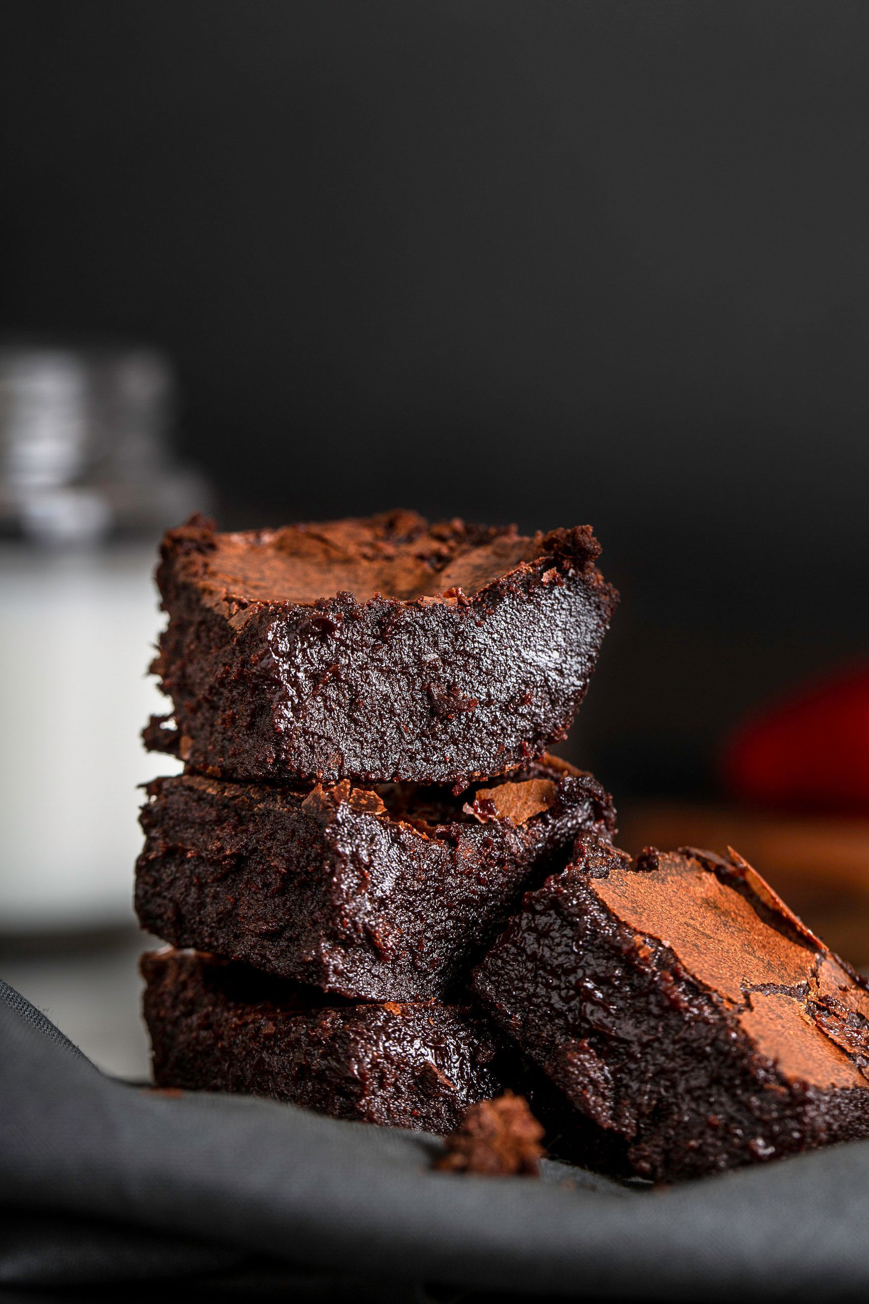 Pilha de brownies de chocolate bem recheados em um prato escuro contra um fundo desfocado.