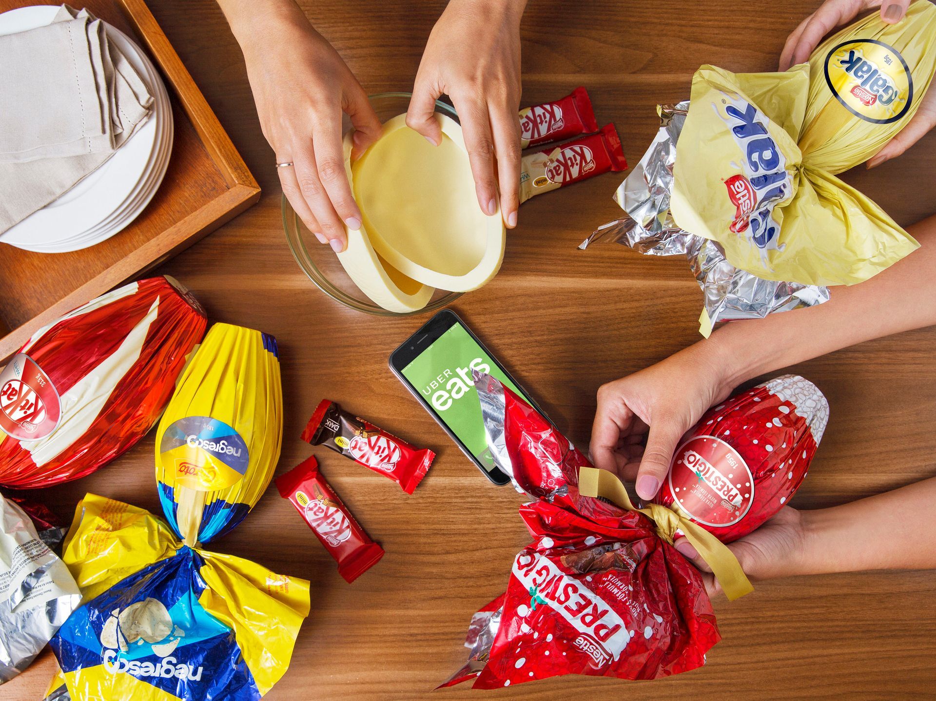 Mãos organizando doces e chocolates embalados em uma mesa de madeira.