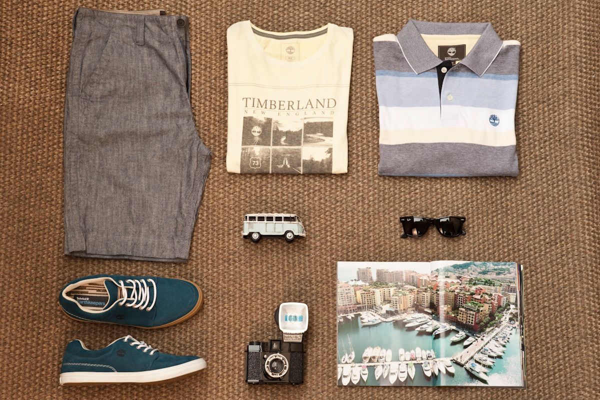 Composição de fotos de viagem com calça cinza, camiseta estampada, polo listrada, tênis verde-azulado, câmera, relógio, óculos de sol, carrinho de brinquedo e cartão-postal.