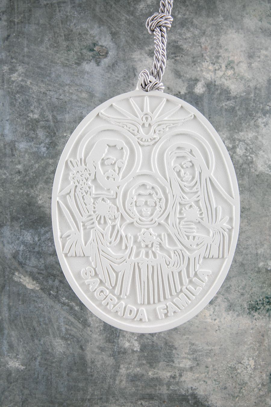Pingente religioso oval branco com figura alada e a palavra “CANADÁ” em uma corrente sobre fundo cinza.