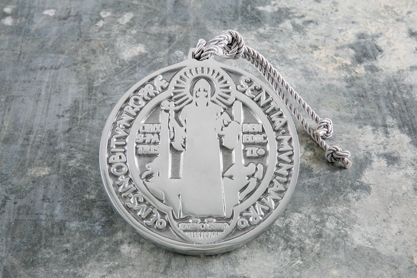 Medalhão religioso branco com a figura de um santo sobre uma parede cinza áspera, parcialmente danificado no canto superior direito.