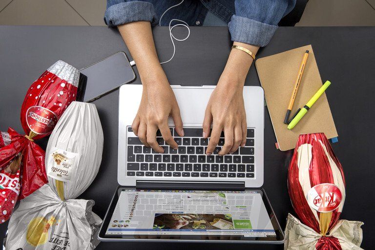 Pessoa digitando em um laptop em uma mesa com lanches, lápis e um caderno ao redor.