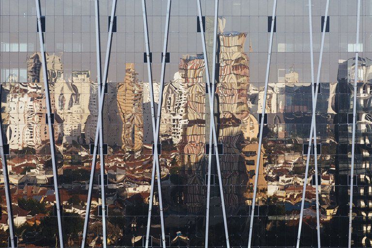 Vista da cidade através da estrutura vertical de um veleiro, com vários arranha-céus ao fundo.