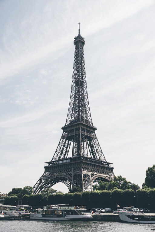 Torre Eiffel em Paris vista do Sena, com barcos e céu nublado.