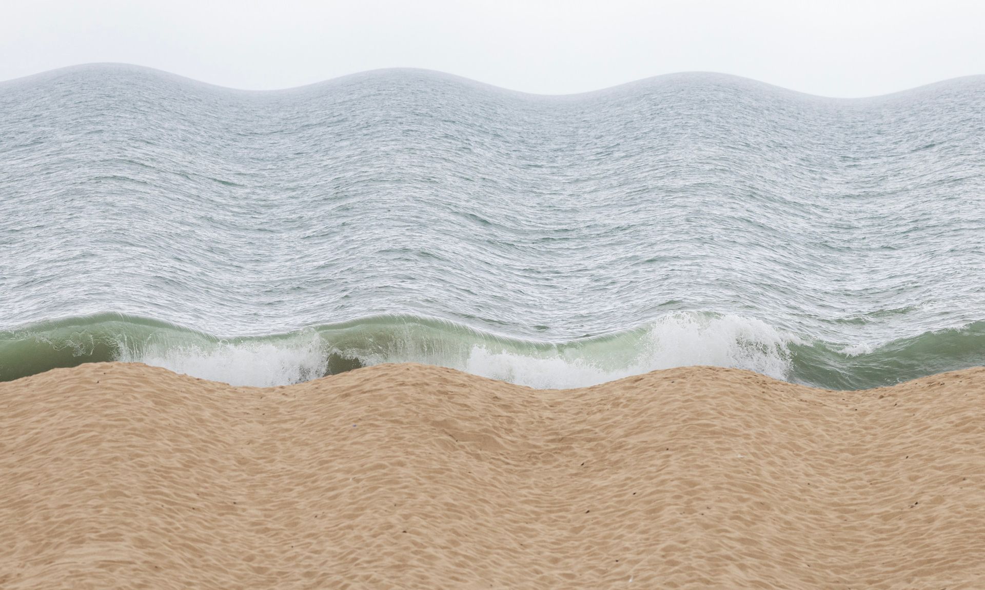 Ondas do oceano encontrando uma praia de areia sob um céu pálido.