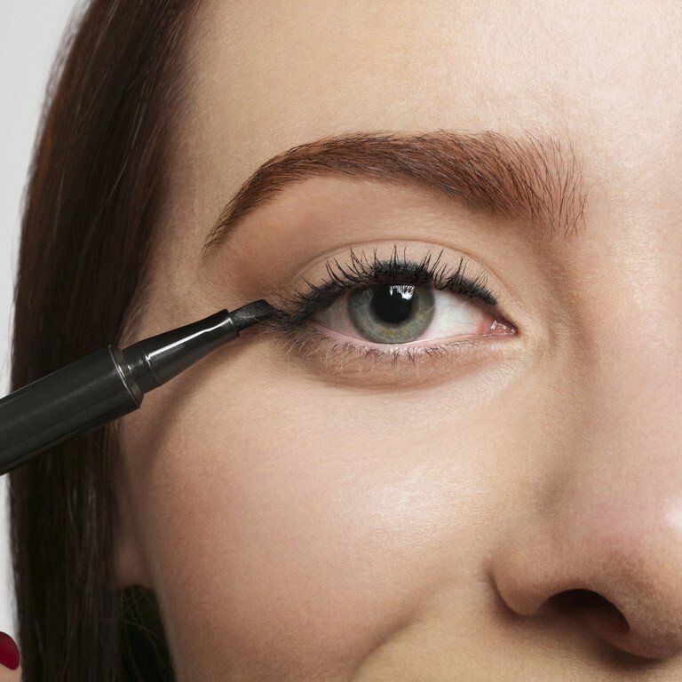 Aplicando rímel em olhos fechados com cílios longos e sobrancelhas bem definidas.