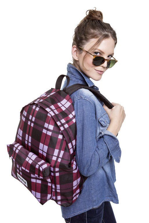 Mulher usando óculos de sol e camisa azul com uma grande mochila xadrez a tiracolo.