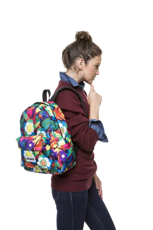 Mulher caminhando de perfil com uma mochila colorida, suéter bordô e calça jeans.