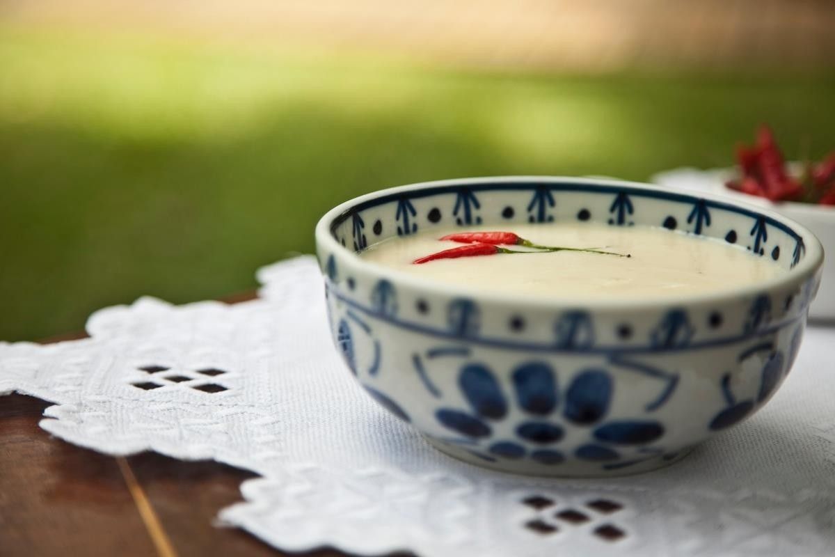 Tigela de cerâmica azul e branca com sobremesa cremosa sobre uma toalha de mesa de renda ao ar livre