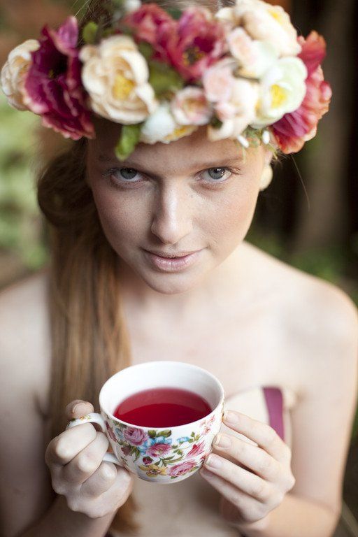 Mulher usando uma coroa de flores segurando uma xícara de chá vermelha florida.