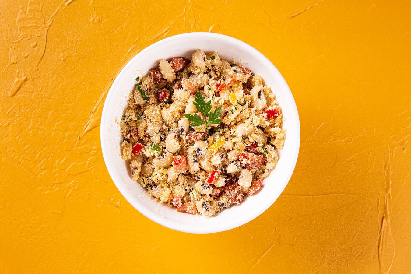 Tigela branca de salada de grãos com ervas sobre um fundo amarelo vibrante.