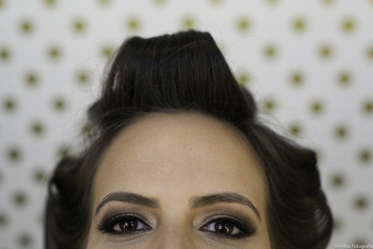 Primeiro plano dos olhos e do cabelo preto penteado de uma pessoa contra um fundo pontilhado.