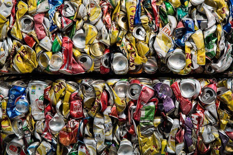 Latas de alumínio prensadas empilhadas em fileiras coloridas, mostrando a reciclagem de metal triturado nas cores vermelho, amarelo, prateado e azul.