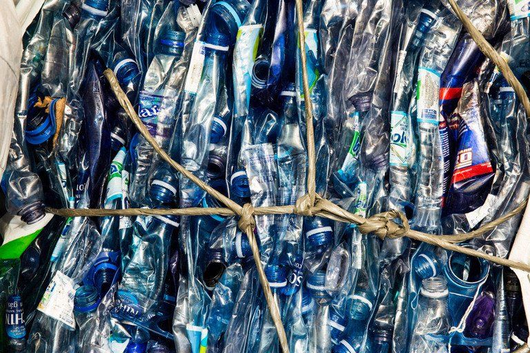 Garrafas de plástico agrupadas e amarradas com corda, separadas para reciclagem em cores azul e transparente.