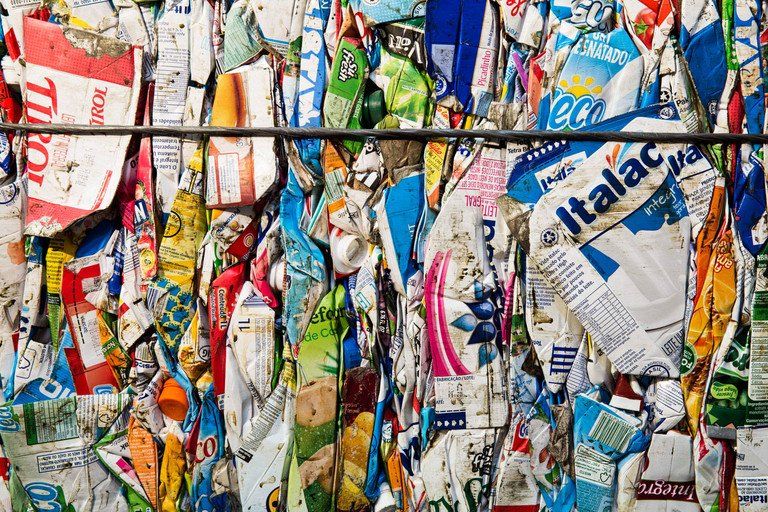 Resíduos plásticos coloridos compactados, agrupados para reciclagem, com etiquetas visíveis e embalagens rasgadas.