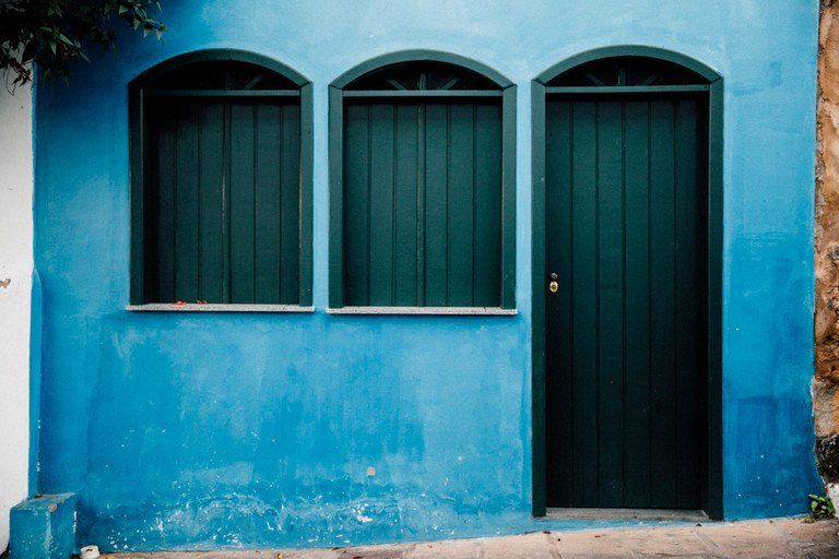 Prédio de estuque azul com três janelas em arco e uma porta preta.