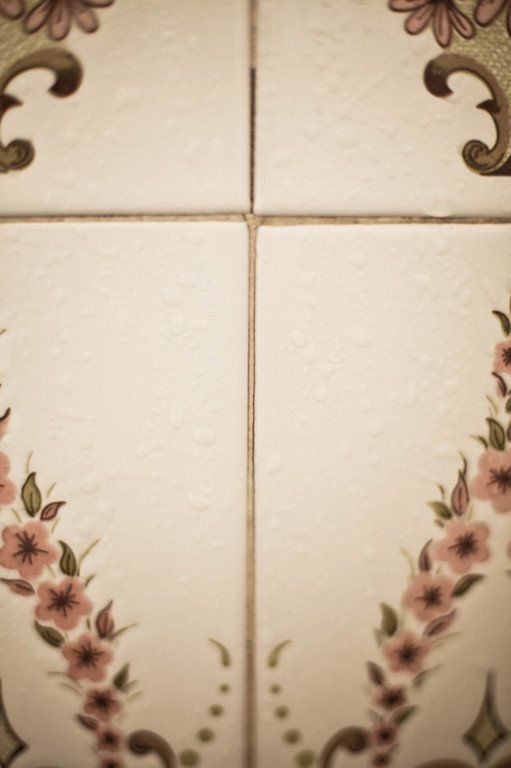 Azulejos decorativos de cerâmica creme com borda floral e detalhes em arabesco marrom nos cantos.