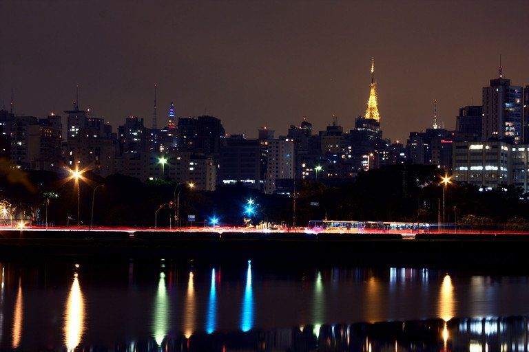 Vista noturna da cidade com arranha-céus iluminados refletidos na água escura.