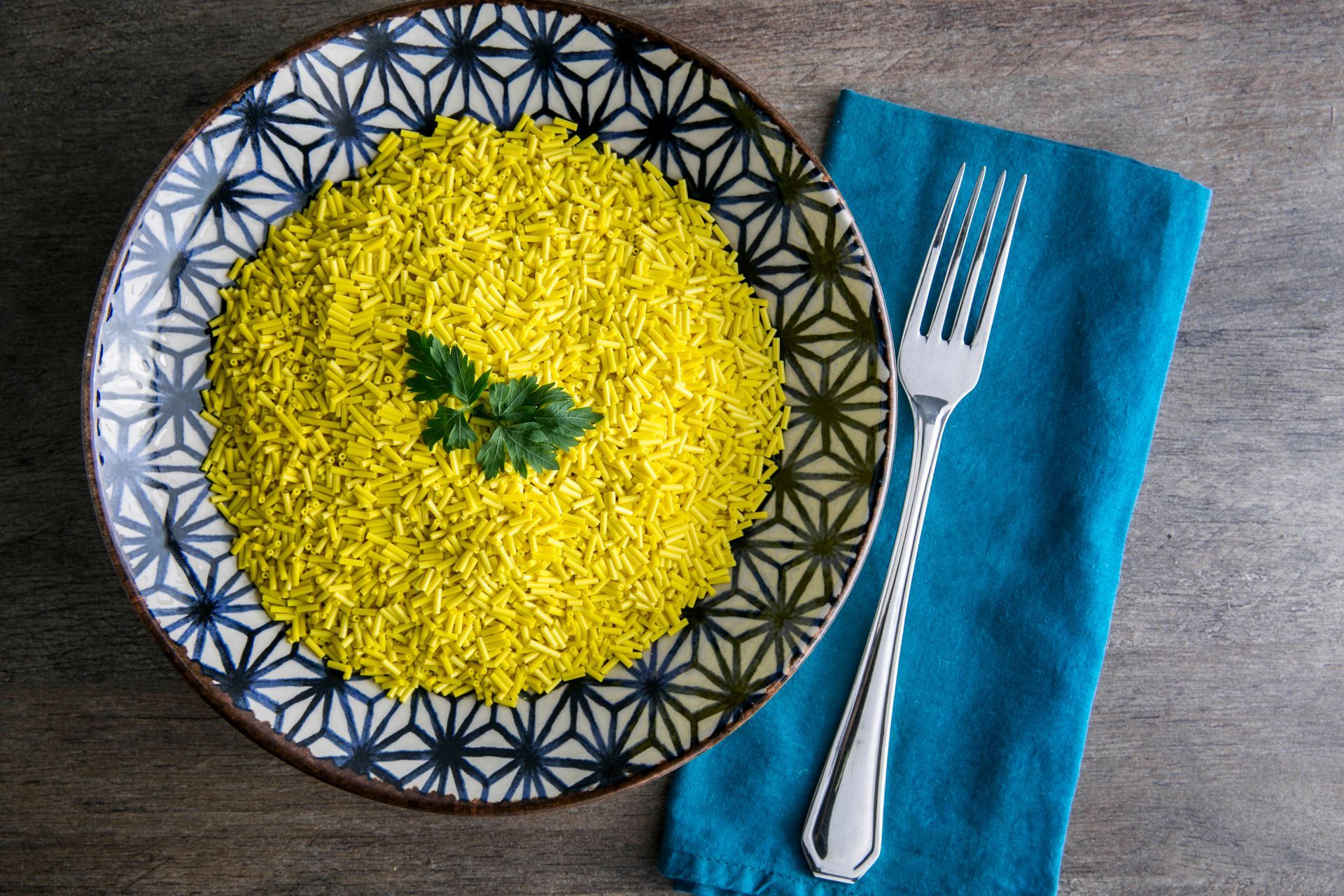 Arroz amarelo em uma tigela estampada com salsa de guarnição, ao lado de um garfo sobre um guardanapo azul.